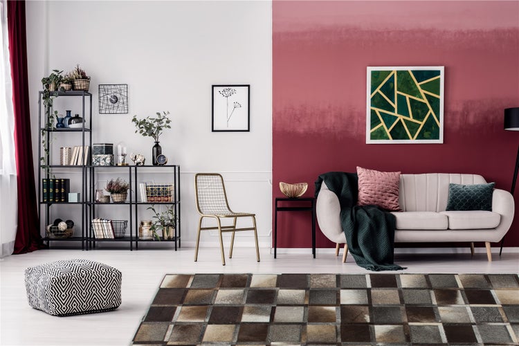 Modernes Wohnzimmer mit zweifarbiger Wand, hellem Sofa, schwarzem Metallregal, goldenem Stuhl und einem Teppich in Patchwork-Optik.