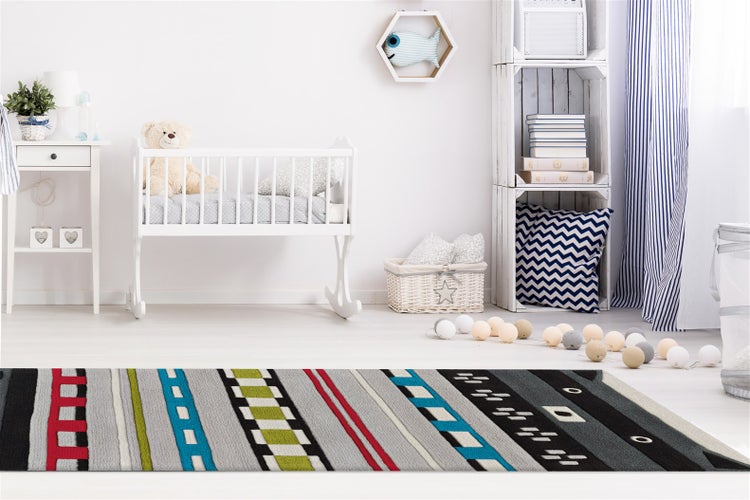 Helles Kinderzimmer mit weißer Wiege und einem bunten Spielteppich mit Straßenmotiven im Vordergrund.