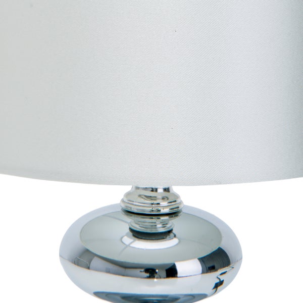 Detailaufnahme einer Tischleuchte mit Lampenschirm und verchromtem Lampenfuß.