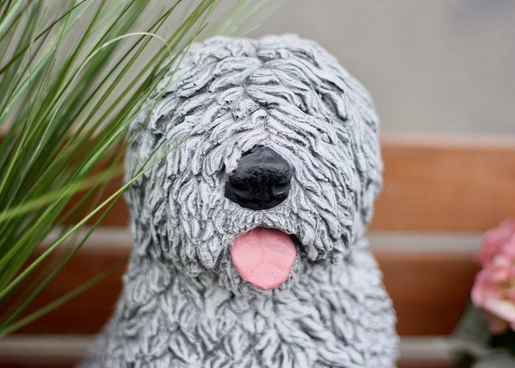 Gartenfigur Hund in Steinoptik mit zotteligem Fell, schwarzer Nase und herausgestreckter Zunge.