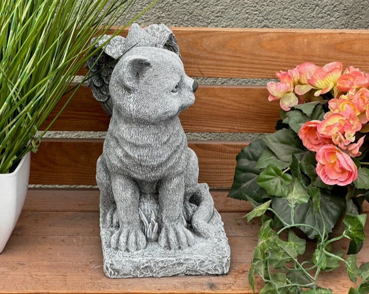 Gartenfigur einer sitzenden Engelkatze in Steinoptik auf einer Holzbank.