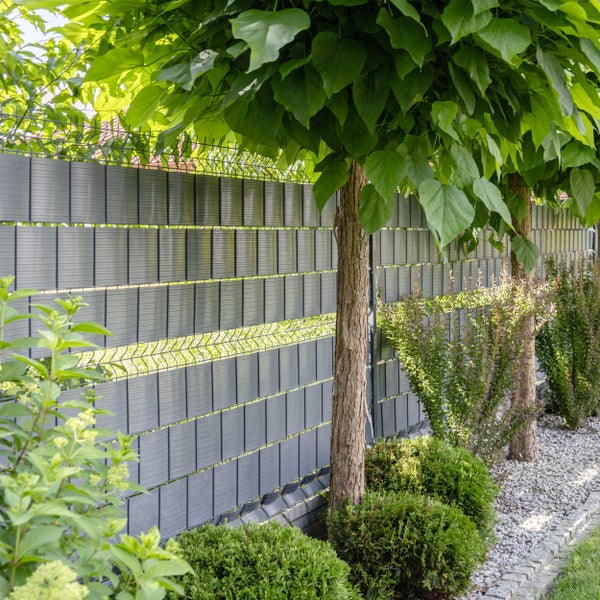 Sichtschutzstreifen in einem Doppelstabmattenzaun im Garten mit Bäumen und Sträuchern als Gestaltungselement