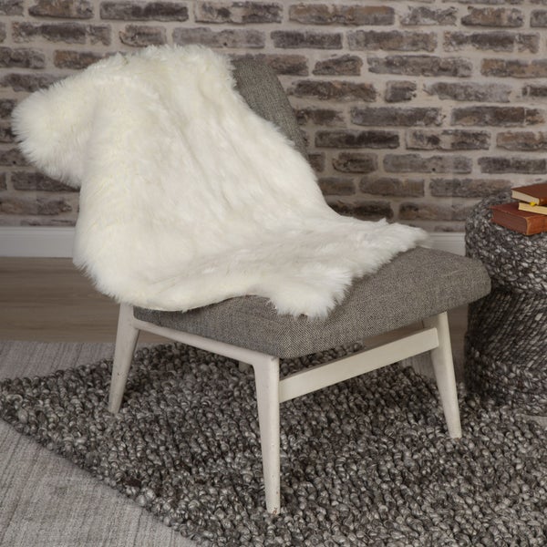 Weißer Kunstfellteppich auf einem grauen Sessel in einem Raum mit Backsteinwand und strukturiertem Teppich.
