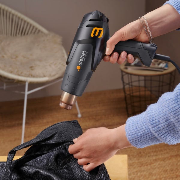 Eine Person verwendet eine Steinel Heißluftgebläse HM 2020 E, um eine schwarze Tasche zu erwärmen.