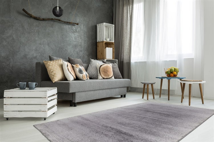 Wohnzimmer mit grauem Sofa, dekorativen Kissen, strukturierter Wand und Couchtisch aus weißer Holzkiste.