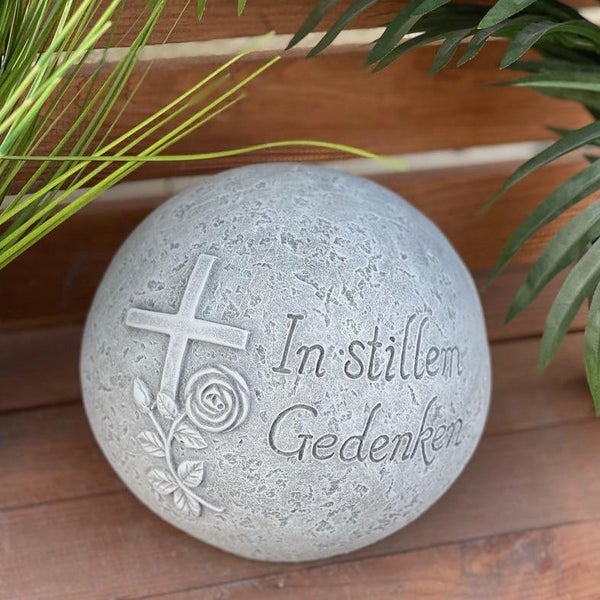 Grabkugel aus Stein mit Kreuz- und Rosenrelief sowie der Inschrift In stillem Gedenken als Grabschmuck