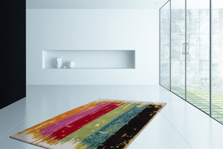 Moderner rechteckiger Teppich mit bunten abstrakten Streifen in einem hellen, minimalistischen Raum mit weißen Wänden und Glasfront.