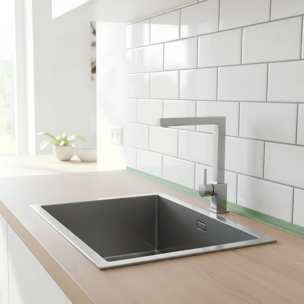 Moderne Küchenspüle aus Edelstahl mit passender Küchenarmatur in einer hellen Küche mit weißen Wandfliesen und Arbeitsplatte in Holzoptik.