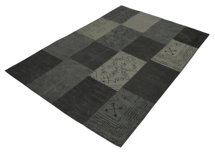 Grauer Patchwork-Teppich mit verschiedenen rechteckigen Feldern, teilweise mit geometrischen Mustern und Symbolen.