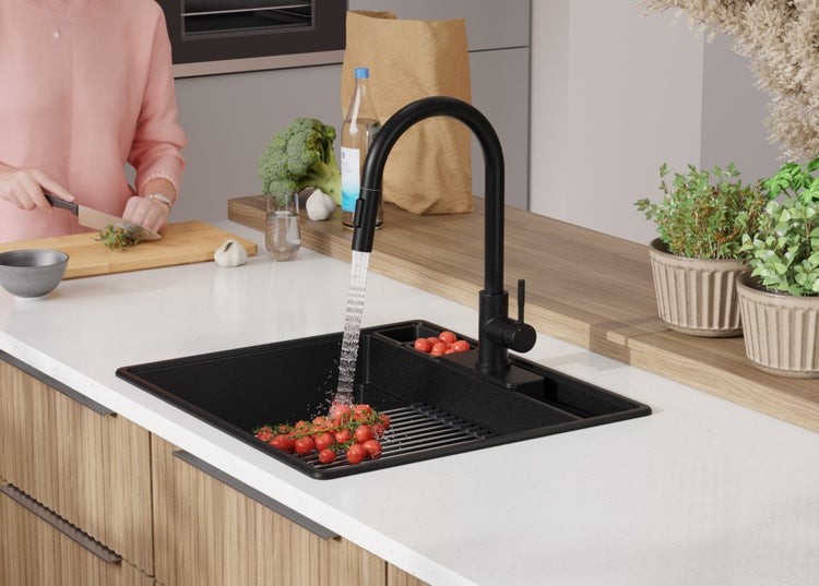 Schwarze Küchenspüle mit Wasserhahn in einer hellen Küche mit Gemüse und Kräutern.