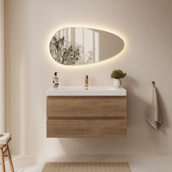 Badezimmer mit hängendem Waschtisch in Holzoptik, weißem Waschbecken, goldener Armatur und asymmetrischem LED Spiegel an der Wand.