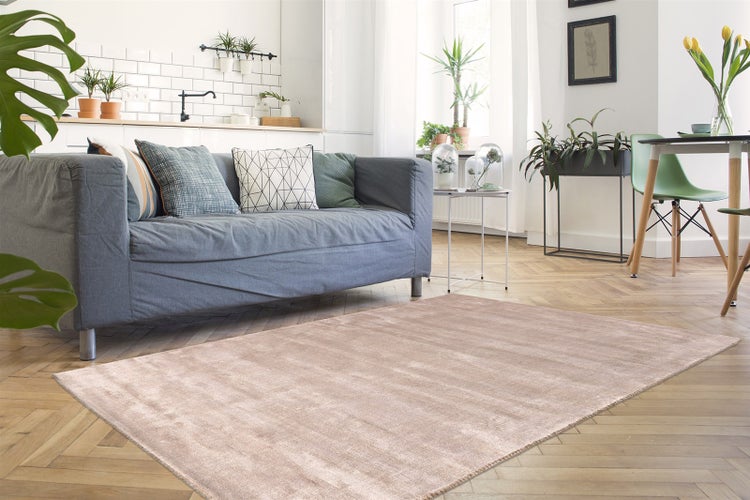 Hellbeiger Teppich in einem hellen Wohnzimmer mit grauem Sofa und Fischgrätparkett.