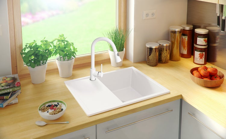 Küchenszene mit weißem Spülbecken, Armatur und verschiedenen Küchenutensilien auf einer hellen Arbeitsplatte.