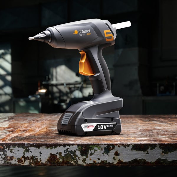 Akku-Heißklebepistole Steinel MG 5011 AMP mit 18 Volt Akku auf einer Werkbank.
