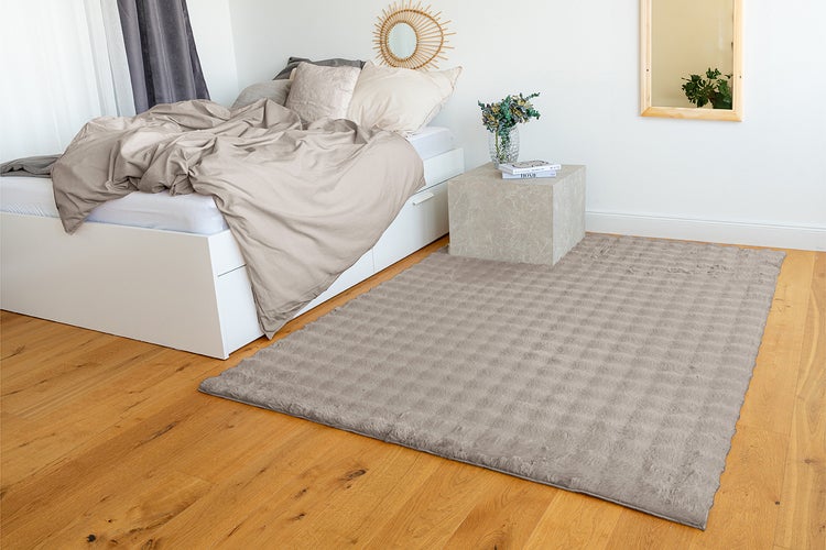 Strukturierter, rechteckiger Teppich in einem hellen Schlafzimmer auf Holzboden neben einem weißen Bett.