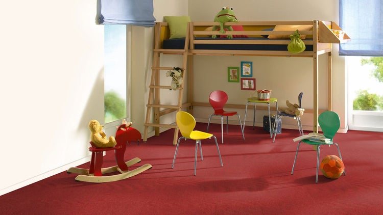 Ein helles Kinderzimmer mit einem roten Teppichboden, einem hölzernen Hochbett, bunten Stühlen und verschiedenen Spielzeugen.