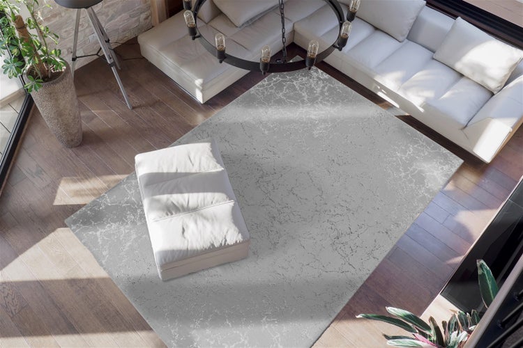 Moderner Wohnraum mit großem Teppich mit Marmormuster, hellem Ecksofa und passendem Hocker auf dunklem Holzboden.