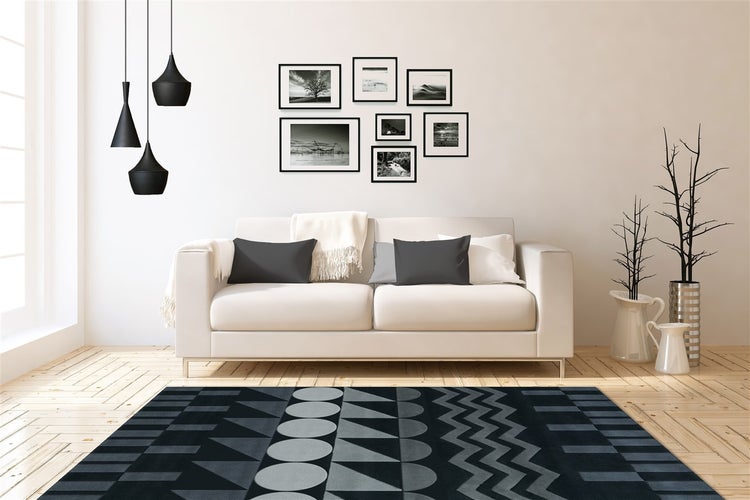Helles Wohnzimmer mit Sofa, Holzboden, schwarz-grauem Teppich mit geometrischem Muster, Bildergalerie an der Wand und schwarzen Pendelleuchten.
