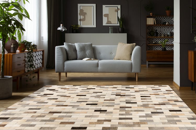 Moderner Wohnraum mit großem Patchwork-Teppich in Rechteck-Optik, grauem Sofa, dunklen Wänden und Holzmöbeln in organisierter Atmosphäre.