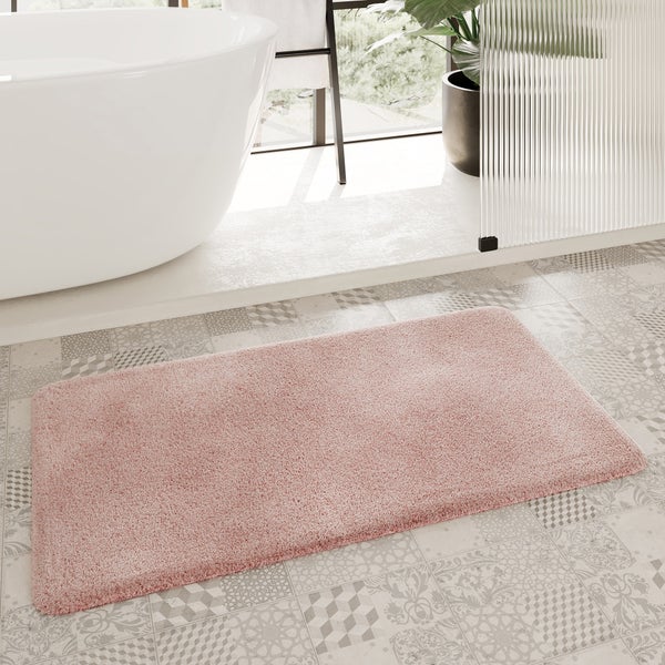 Rechteckige, flauschige Badematte vor einer freistehenden Badewanne in einem hellen Badezimmer mit gemusterten Bodenfliesen.