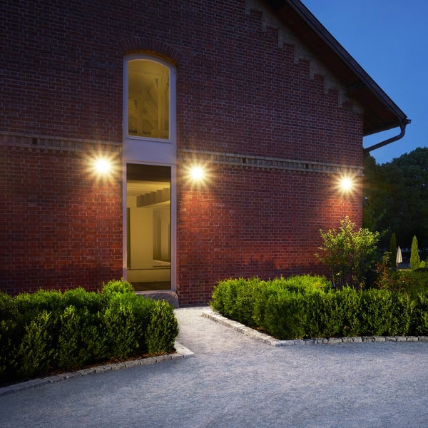 Beleuchtete Ziegelfassade bei Nacht mit drei modernen Außenleuchten die den Weg und den Garten vor dem Haus erhellen.