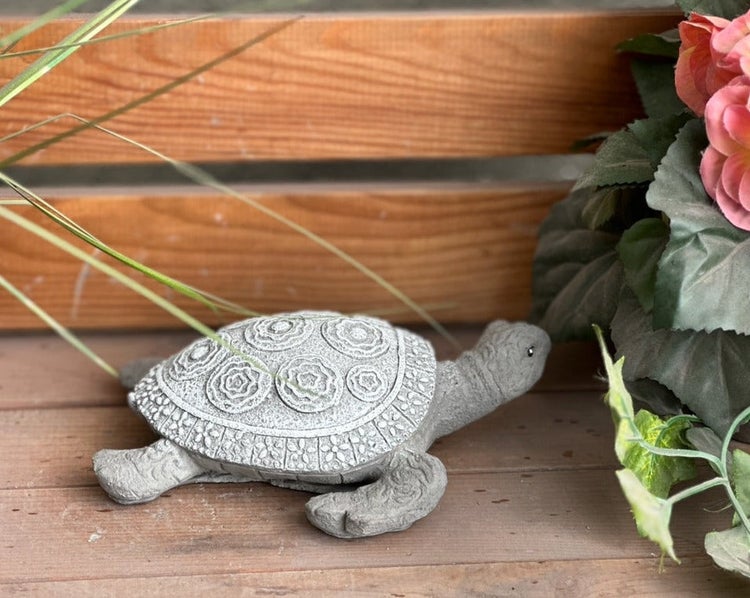 Gartenfigur Schildkröte aus Steinguss mit gemustertem Panzer, platziert auf Holz neben Pflanzen.