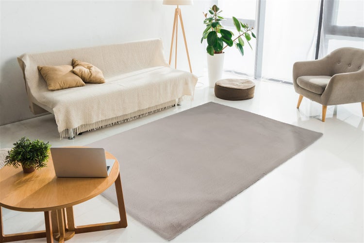 Hellbrauner, rechteckiger Teppich in einem hellen, modern eingerichteten Wohnzimmer mit Sofa, Sessel und Holz-Couchtisch.