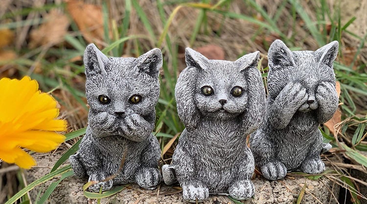 Drei Katzenstatuen aus Stein in der Pose nichts hören, nichts sehen, nichts sagen auf einem Stein im Garten platziert.