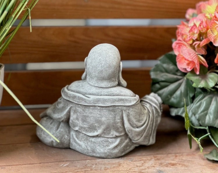 Rückansicht einer kleinen, sitzenden Buddha-Dekofigur in Steinoptik auf Holzgrund.