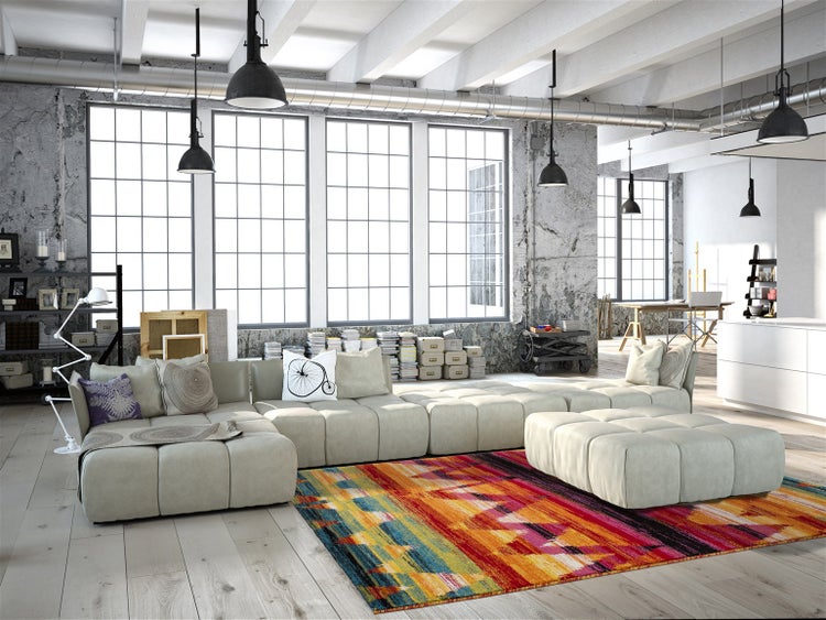 Wohnzimmer im Industriestil mit großem modularem Sofa, bunt gemustertem Teppich, Sichtbetonwänden und großen Fenstern.