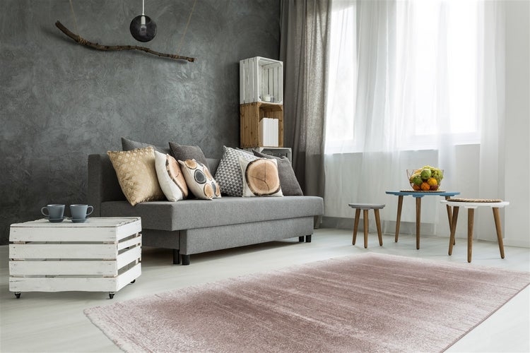Modernes Wohnzimmer mit grauem Sofa, Zierkissen, einem rosa Teppich, einer strukturierten dunkelgrauen Wand und Beistelltischen aus Holz.