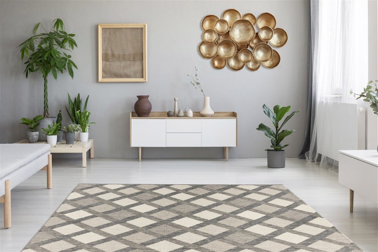 Moderner Wohnraum mit grau-cremefarbenem Teppich im Rautenmuster, weißem Sideboard, Zimmerpflanzen und goldener Wanddekoration auf grauer Wand.