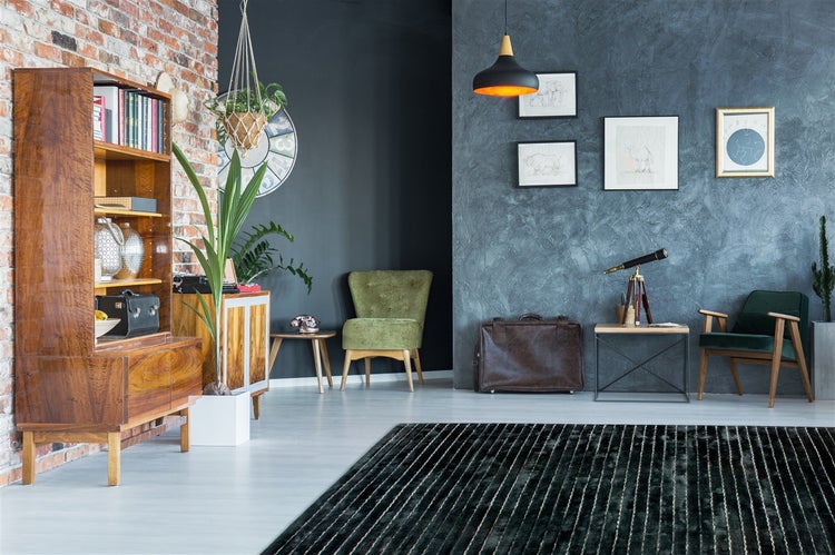 Modernes Wohnzimmer mit Backsteinwand, dunkelgrauer Strukturwand, Holzschrank, grünen Sesseln und einem dunkel gestreiften Teppich.