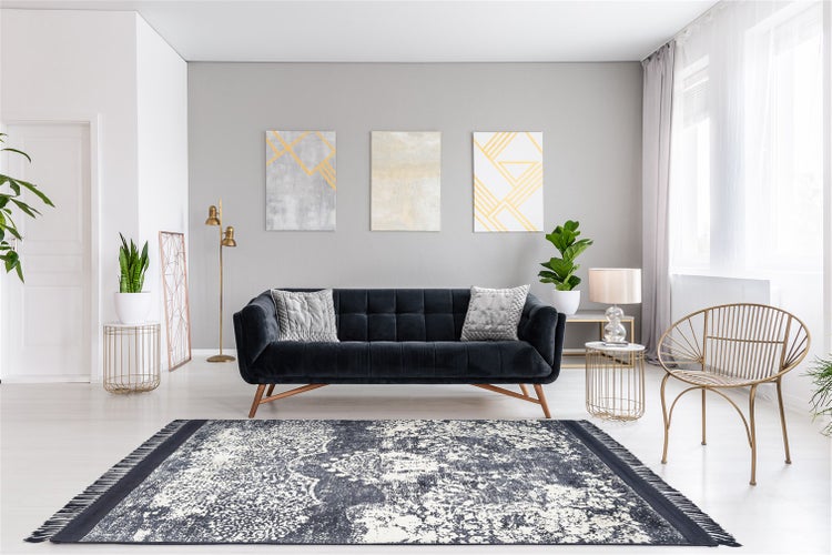 Modernes Wohnzimmer mit dunklem Samtsofa, gemustertem Teppich, abstrakten Wandbildern und goldenen Metallelementen in hellem Ambiente.