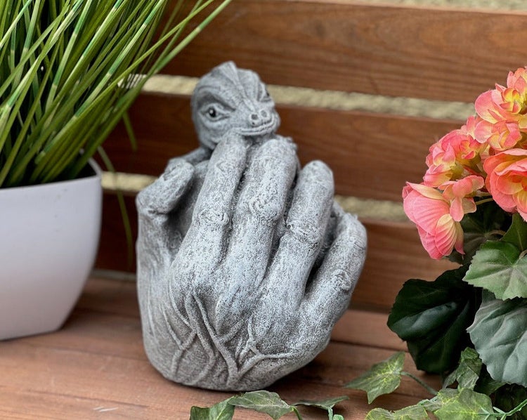 Gartendekoration aus Steinguss: Eine Hand, die einen kleinen Drachen hält.