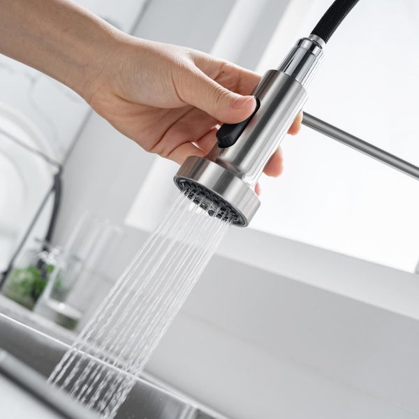 Eine Hand hält eine ausziehbare Küchenarmatur mit herauslaufendem Wasserstrahl über einer Edelstahlspüle.
