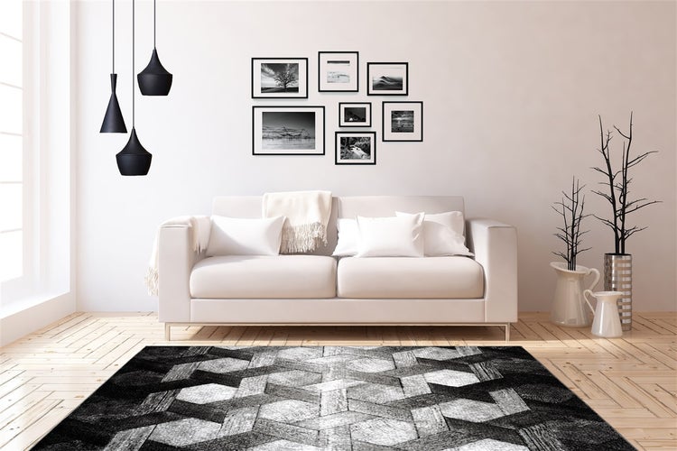 Modernes, helles Wohnzimmer mit einem Teppich mit schwarz-grauem geometrischem Muster auf hellem Parkettboden, weißem Sofa und schwarzen Pendelleuchten.