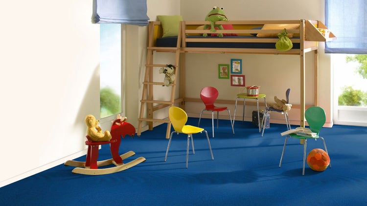 Hell eingerichtetes Kinderzimmer mit blauem Teppichboden, einem Hochbett aus Holz, bunten Stühlen und einem Schaukelpferd.