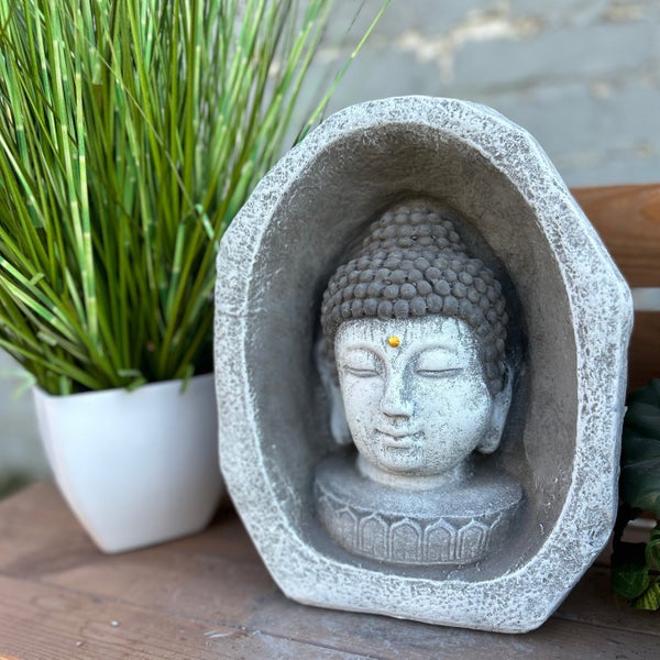 Buddha-Kopf in einer Steinnische als Gartendekoration neben einer Pflanze im Topf