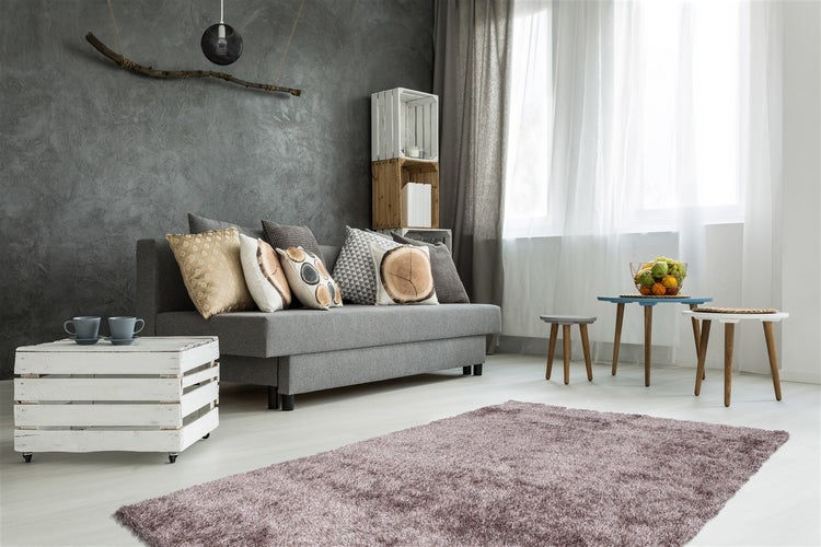 Modernes Wohnzimmer mit grauem Sofa, dunklem Wandputz mit Struktur, flauschigem Teppich, Couchtisch aus Holzkiste und hellen Vorhängen.