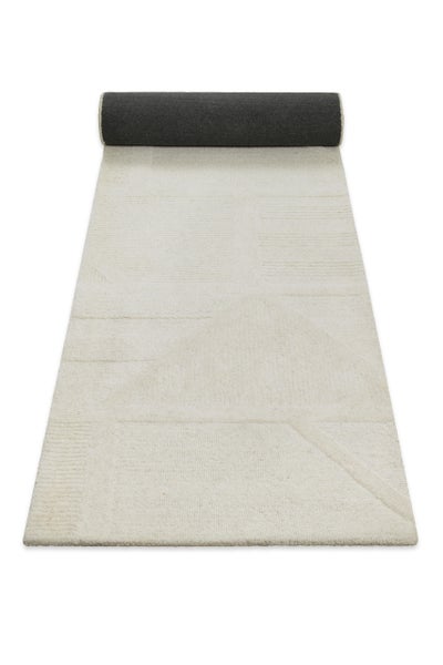 Strukturierter Teppichläufer mit geometrischem Muster in Creme, am oberen Ende teilweise aufgerollt.