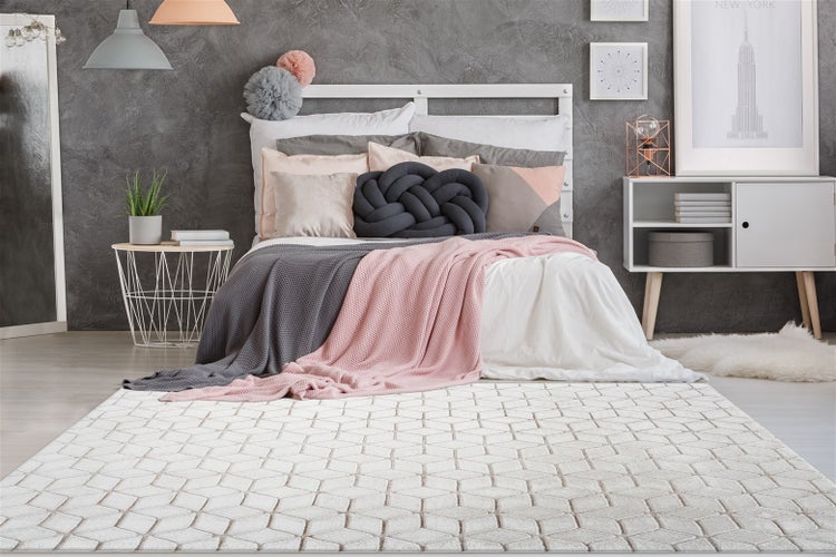 Moderner Teppich mit geometrischem Muster in einem Schlafzimmer mit Bett, strukturierter Wand und dekorativen Kissen.