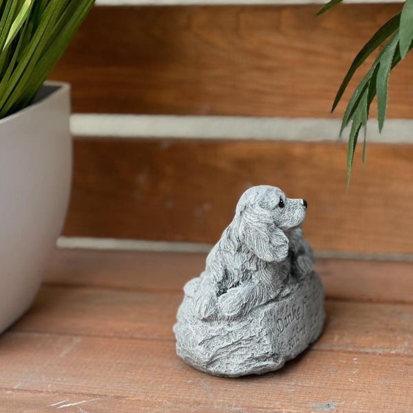 Dekorative Gartenfigur in Form eines sitzenden Hundes aus Steinoptik mit der Inschrift Danke für die schöne Zeit auf einem Holzuntergrund.