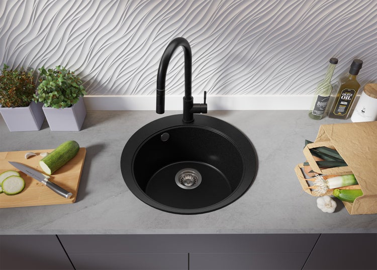 Schwarze Küchenspüle mit Armatur auf einer Küchentheke mit Gemüse.