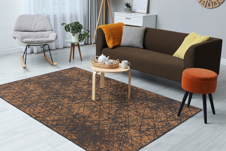 Modernes Wohnzimmer mit rechteckigem Teppich mit abstraktem Linienmuster, dunklem Sofa mit Kissen, Couchtisch und hellem Bodenbelag.