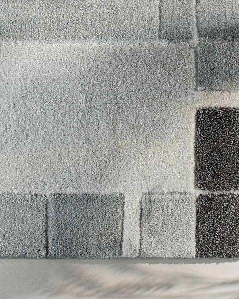 Hochflor-Teppich mit geometrischem Muster aus Quadraten in verschiedenen Grautönen.