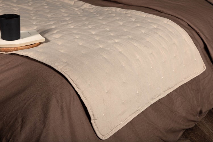 Gesteppter Bettläufer beige mit Punktmuster, ausgebreitet auf einer braunen Tagesdecke.