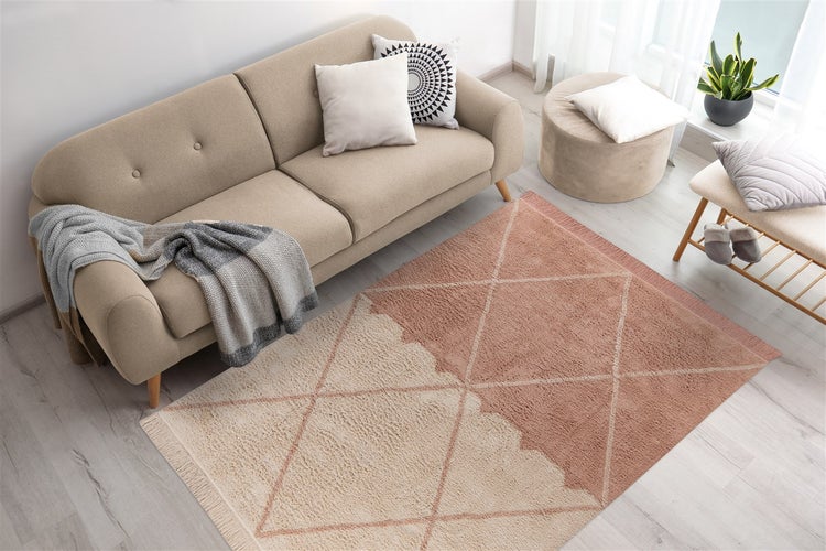 Helles Wohnzimmer mit einem zweifarbigen Teppich mit geometrischem Rautenmuster und Fransen, einem Sofa, Kissen und einem Pouf.