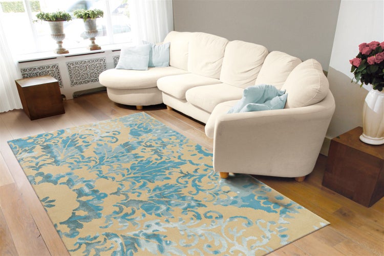 Helles Wohnzimmer mit blau-beige gemustertem Teppich auf Holzfußboden, einem großen cremefarbenen Ecksofa und Beistelltischen aus Holz.