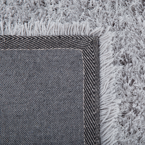 Detailansicht eines grauen Hochflorteppichs mit Fransen und gewebter Rückseite